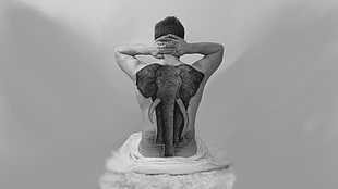 grayscale photo of man sitting with elephant tattoo on back