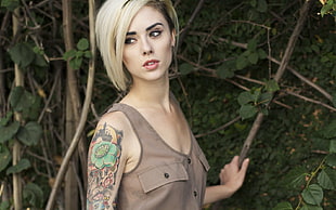 blonde haired female in brown sleeveless top holding tree branch during daytime
