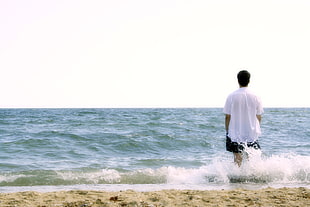 man wearing white shirt standing beside the beach