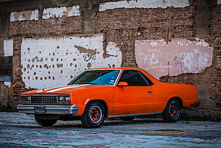 orange Chevrolet El Camino parked beside brown brick wall