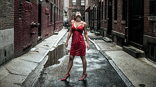 woman with red spaghetti strap dress standing between brown building
