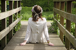 woman wearing white lace dress sitting on wooden bridge