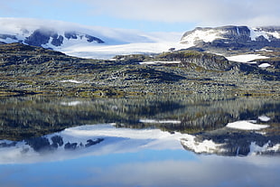 green grasses beside body of water surrounded with snow ground mountain during daytime, norway