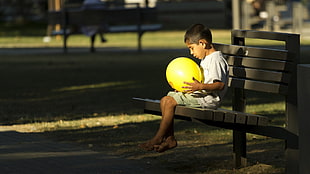 boy in white shirt sitting on bench holding yellow balloon