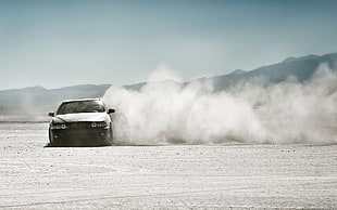 white vehicle running on gray sand with ash