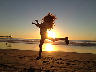 silhouette photo of girl jumping on sand near sea shore during golden houre HD wallpaper