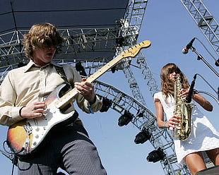 man and woman performing guitar and trombone on stage during daytime