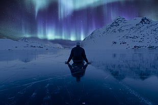 man sitting on frosted lake watching Norther Aurora lights
