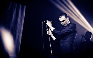 man in black suit jacket standing on stage holding microphone