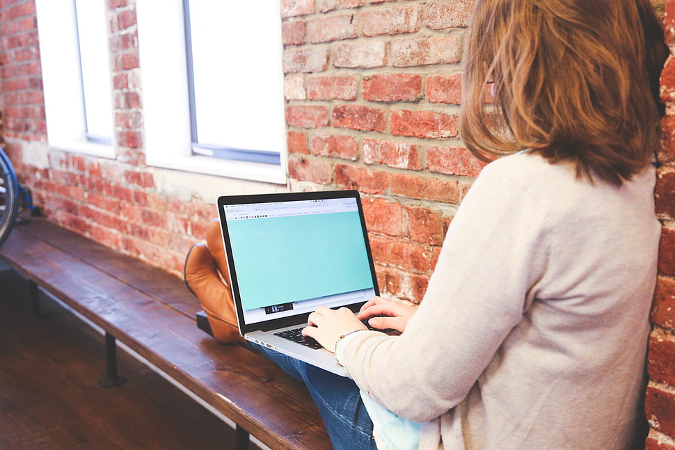 woman sitting near brick wall while using her laptop HD wallpaper