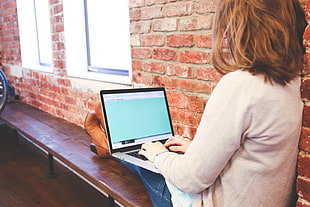 woman sitting near brick wall while using her laptop