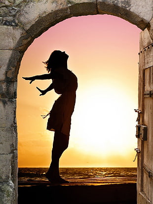 photo of woman standing near arc window during golden hour