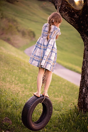 girl standing on swing tire under tree