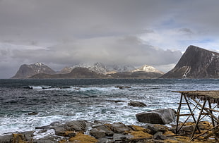 rocky seashore in front of gray mountains and clouds during daytime