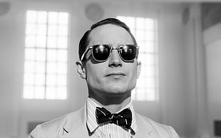 gray-scale photo of man in gray formal suit attire wearing clubmaster sunglasses