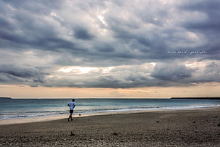 man walking on seashore under blue cloudy skies