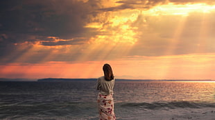 photography of woman in gray dress near body of water during sunset