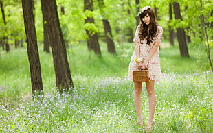 woman wearing beige dress holding brown wicker basket standing on green grass