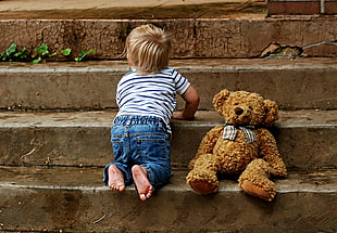 child in blue and white stripe short-sleeved top and blue pants with brown bear plush toy in stairs