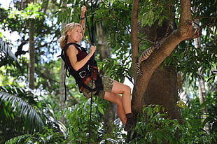 woman climb using rope near tree with brown animal at day time
