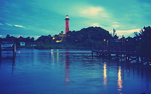 red lighthouse with lights on during twilight