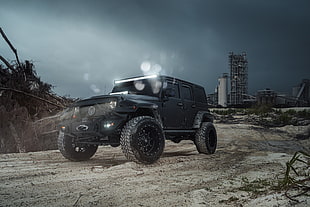black Jeep Wrangler on brown road with view of concrete building