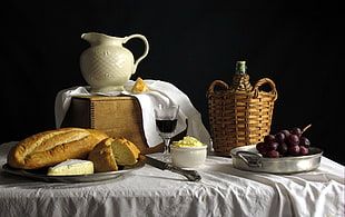 slice loaf with glass of wine. grapes, basket and pitcher on table set