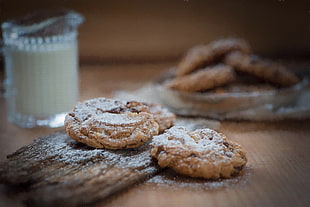 selective focus photography of cookies beside clear glass mug filled with white liquid on brown surface