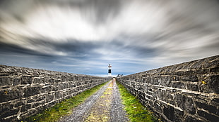 timelapse photography of pathway in between concrete walls and lighthouse range view, ireland