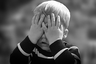 toddler boy in black and white stripe covering face in greyscale photography