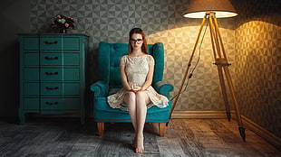 woman wearing white floral mini dress sitting on green sofa between brown floor lamp and green tallboy dresser