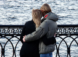 couple embracing while looking at body of water during daytime