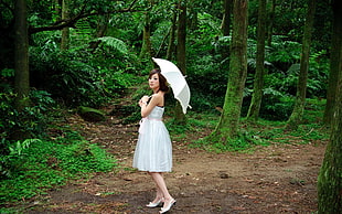 woman wearing white mini dress holding umbrella in forest