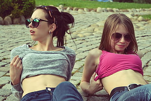 two women in gray and pink crop tops leaning on gray concrete bricks
