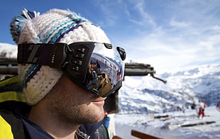 man wears black snow goggles and white and blue bubble hat