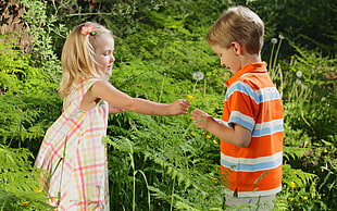 girl giving boy's yellow Dandelion flower beside woods