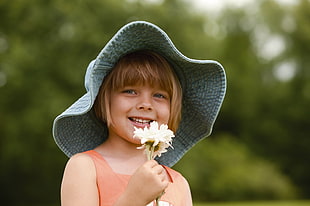 girl in gray bucket hat holding white cluster flower during daytime