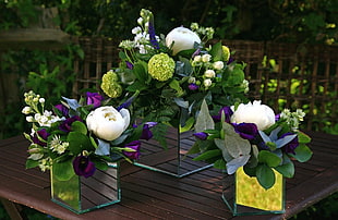 white and purple flowers in clear glass vases on top of brown wooden table