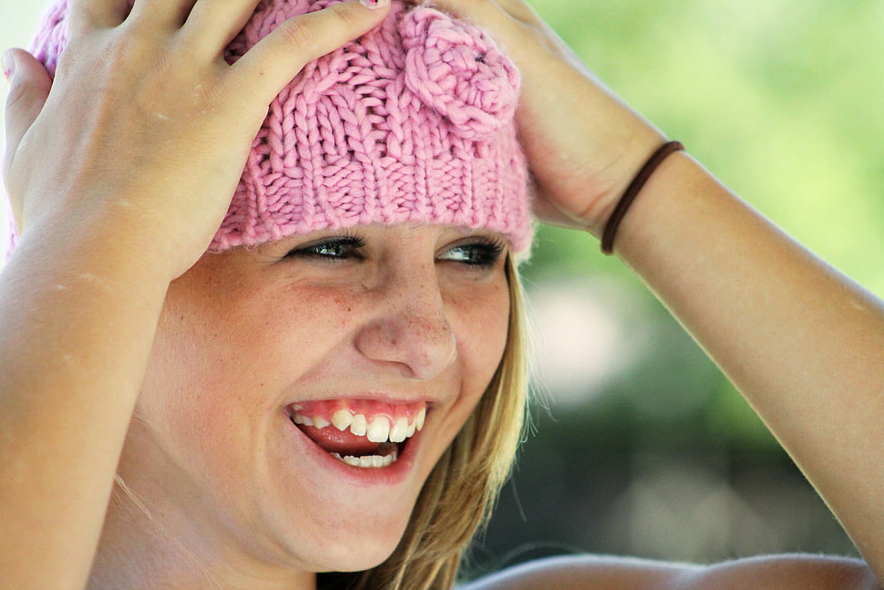 smiling blonde haired holding and wearing pink cable-knit cap HD wallpaper