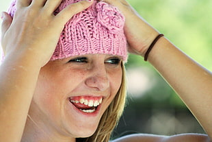 smiling blonde haired holding and wearing pink cable-knit cap