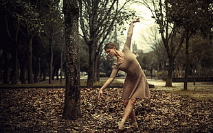 woman wearing brown dress dancing on ground with dried leaves near tree