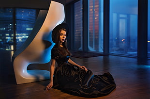 woman in black dress beside chair near glass wall