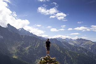 man in black t-shirt standing on mountain cliff under blue sky