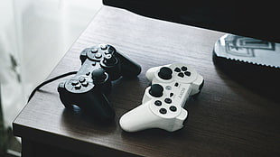 two black and white Sony PS3 controllers on brown wooden table