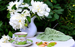 white peony flower in vase at table near teacup with saucer