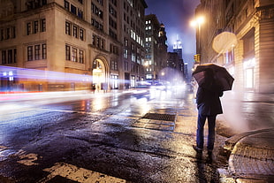 time lapse photo of person holding umbrella in middle of road during nighttime, empire
