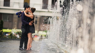 photography of couple in black and blue suit kissing near water fountain at daytime HD wallpaper