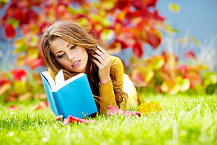 selective focus photography of woman reading book while lying on ground