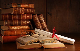 pile of brown hardbound books, books, ribbon, paper, glasses