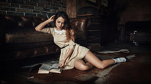 woman lying on floor leaning on brown leather sofa holding opened book